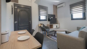 A compact living space with a dining area, a sofa, a TV, and a kitchenette. - Asteria Mare 1 by Travel Pro Services (Polygyros)