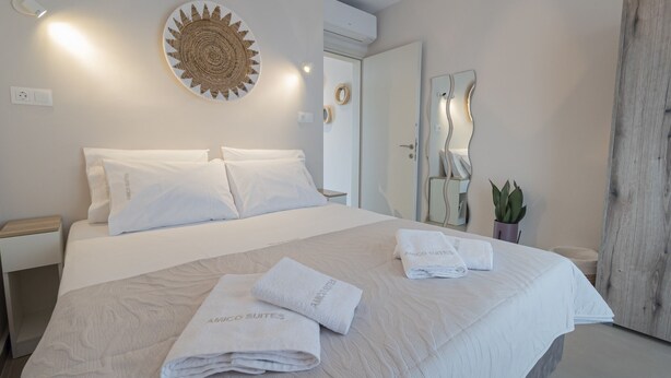 Une chambre d’hôtel avec un grand lit, deux oreillers, une table de chevet, un miroir fixé au mur, un élément décoratif mural et une plante en pot.