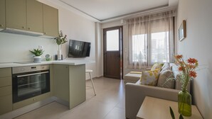 Une cuisine moderne dotée d’un four encastré, un coin repas avec une table et des chaises, et un salon avec un canapé et un téléviseur.