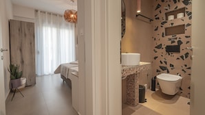 Une salle de bain moderne avec des toilettes, un lavabo et une douche. Il y a une plante dans le coin et un rideau dans la pièce adjacente.