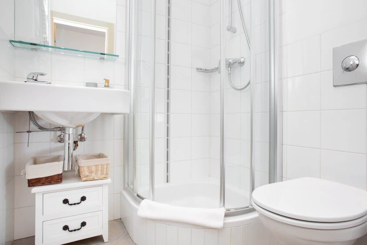 A modern bathroom with a glass shower enclosure, a white sink with a glass shelf, and a white toilet.