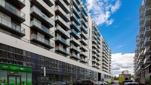 A modern apartment building with balconies, a cafe named 'Zabka cafe' on the ground floor, and a clear blue sky.