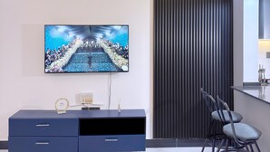 A modern living room with a flat-screen TV mounted on the wall, a dark blue entertainment unit with drawers, a tall black acoustic panel, and a pair of bar stools. - B&S Luxe Living (Kampala)