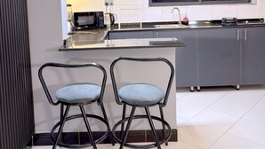 A modern kitchen with grey cabinets, a large island with a sink, and two bar stools. - B&S Luxe Living (Kampala)