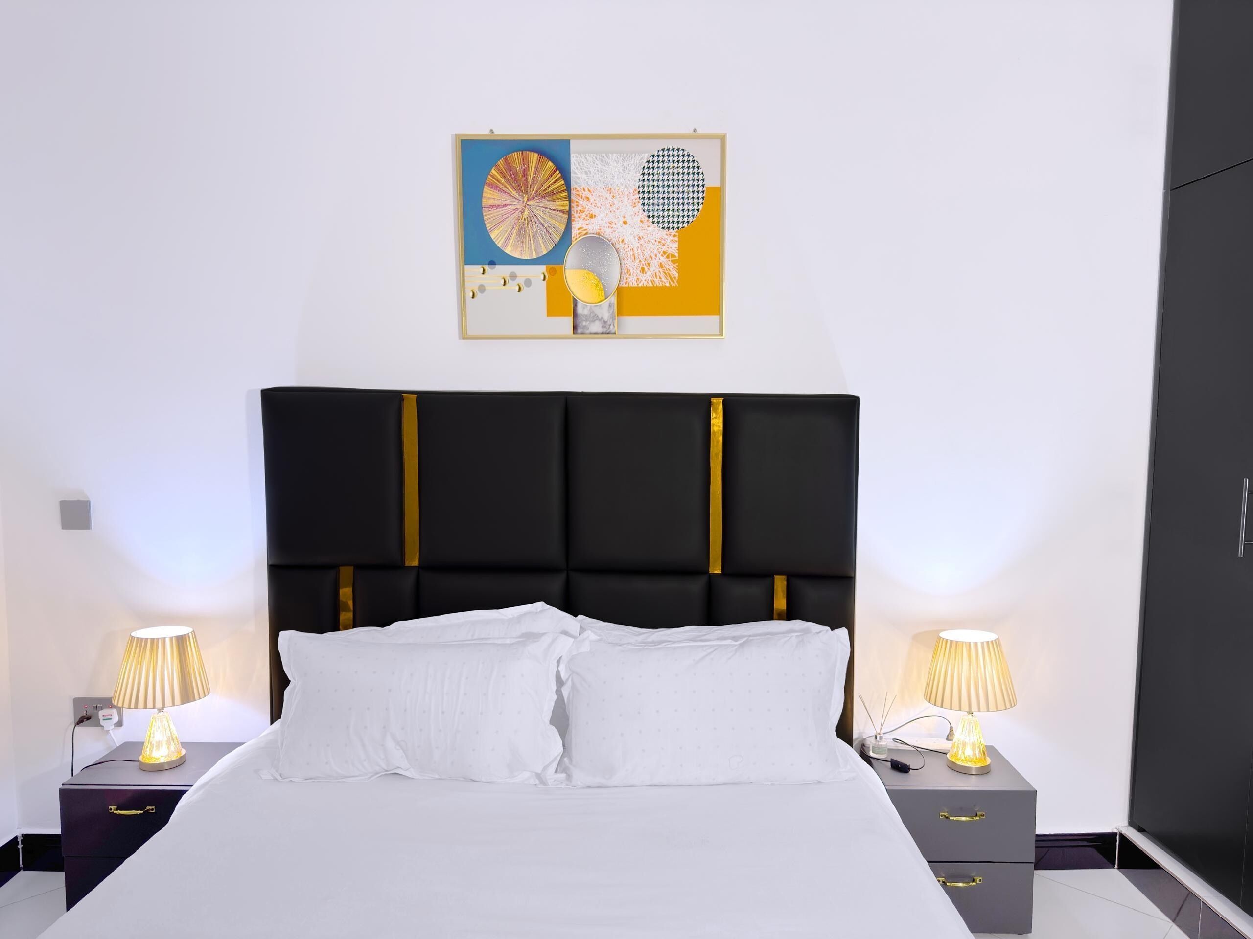 A modern bedroom with a black headboard, white bedding, and two bedside tables with lamps.