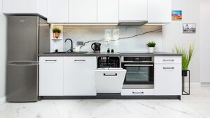 Eine moderne Küche mit weißen Schränken, einem Edelstahlkühlschrank, einer Spülmaschine und einem Backofen.
