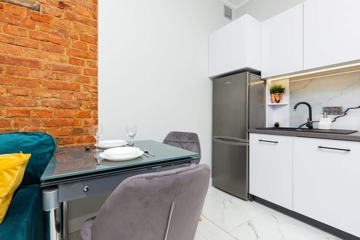 A compact kitchen with white cabinets, a stainless steel refrigerator, and a small potted plant on the countertop.
