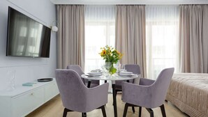 Ein modernes Hotelzimmer mit Essbereich, einem Bett und einem an der Wand montierten Fernseher.