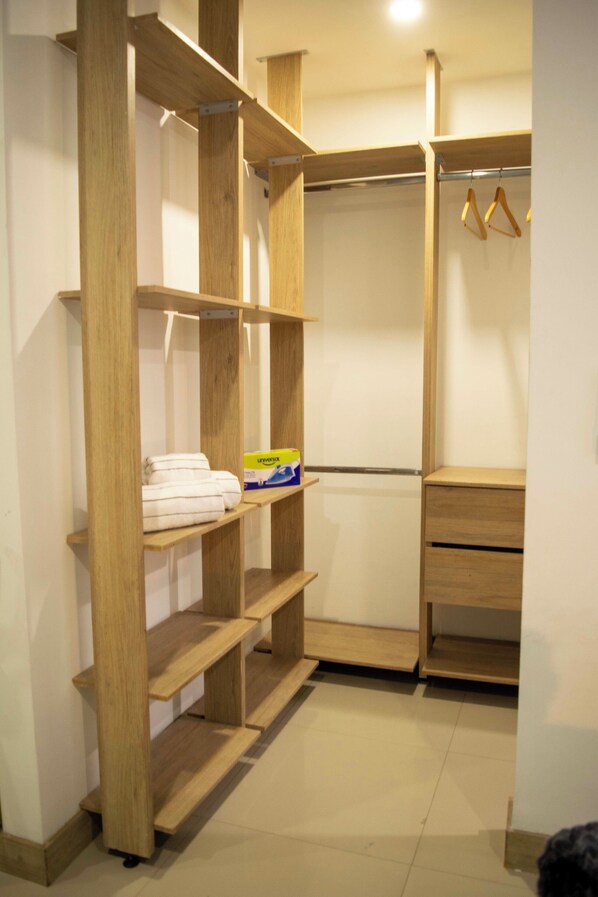 A walk-in closet with wooden shelving, a hanging rod, and a small storage unit. - Migar Alojamientos (Cali)