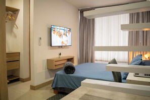 Una camera d'albergo con un letto, una televisione montata a parete, un comodino con una lampada e una finestra con tende.