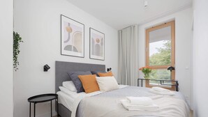 A modern bedroom with a bed, a bedside table, a window with curtains, and two framed pictures on the wall.