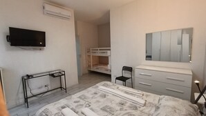 A bedroom with a bed, a TV, a dresser, a mirror, and a bunk bed in the background.