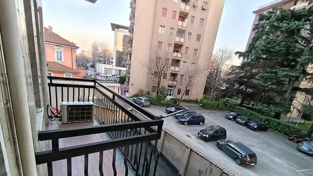 A balcony with a view of a parking lot and surrounding buildings.