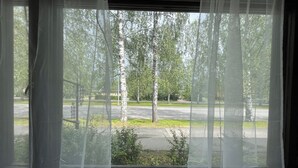 A window with sheer curtains, a view of a street with trees, and a sign with numbers. - 2-bedroom flat with own garden (Helsinki)