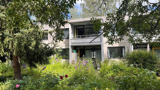 A modern building with a balcony, surrounded by lush greenery and various plants. - 2-bedroom flat with own garden (Helsinki)
