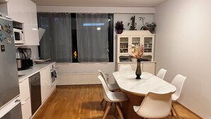 A modern kitchen with white cabinetry, a dining table with chairs, a microwave, and a window with curtains. - 2-bedroom flat with own garden (Helsinki)
