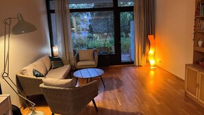 A modern living room with a sofa, chairs, a small table, and a large window with curtains. - 2-bedroom flat with own garden (Helsinki)