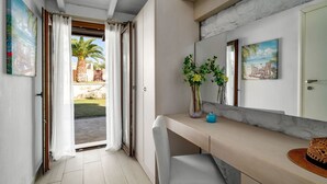 A modern interior with a sliding glass door leading to a patio, a white chair, a small table, and a vase with flowers. - Palmrise Luxury Villas - Helios Villa (Kassandra)