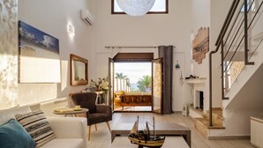 A spacious living room with a sofa, armchair, and coffee table. A large window offers a view of the outdoors. - Palmrise Luxury Villas - Helios Villa (Kassandra)