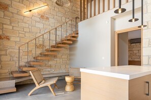 Ein modernes Interieur mit einer Steinwand, einer Holztreppe und einer Küchenzeile mit weißer Arbeitsplatte.
