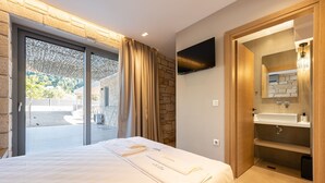 A modern hotel room with a bed, a bathroom with a sink and mirror, and a sliding glass door leading to an outdoor area.