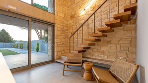 A modern interior with a stone wall staircase, a glass door leading outside, and two wicker chairs.