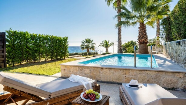 A poolside area with lounge chairs, a table with a plate of grapes, and a view of the sea. - Palmrise Luxury Villas - Maistros Villa (Kassandra)