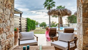 A patio with wooden furniture, a glass table, and a view of a pool and palm trees. - Palmrise Luxury Villas - Maistros Villa (Kassandra)
