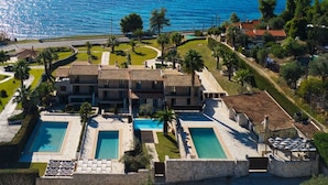 A coastal hotel with multiple swimming pools, a road in the foreground, and a view of the sea and mountains in the background. - Palmrise Luxury Villas - Maistros Villa (Kassandra)