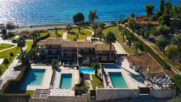 Ein Hotel an der Küste mit mehreren Swimmingpools, einer Straße im Vordergrund und Blick auf Meer und Berge im Hintergrund.