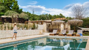 Ein Poolbereich mit Liegestühlen, einer Steinmauer und einer Pergola mit einem Reetdach.