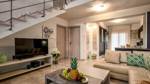 A modern living room with a TV, a coffee table with fruit, a sofa, and a staircase. - Palmrise Luxury Villas - Anemos Villa (Kassandra)