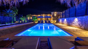 A swimming pool with lounge chairs and umbrellas, surrounded by a stone wall and palm trees. - Palmrise Luxury Villas - Anemos Villa (Kassandra)