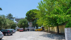 A parking area with several cars, a yellow car, and a building with a balcony in the background.