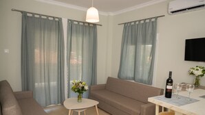 A living room with a sofa, a small table with a vase of flowers, a dining table with chairs, and a flat-screen TV mounted on the wall.