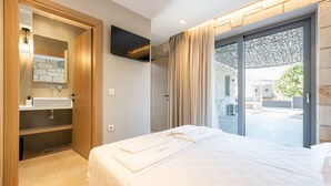 Ein modernes Hotelzimmer mit einem großen Bett, einem fest eingebauten Waschbecken, einem Flachbildfernseher und einer Schiebeglastür zu einem Außenbereich.