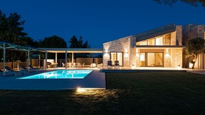 Ein modernes Haus mit Swimmingpool, Natursteinhausfassade und Sitzbereich im Freien.