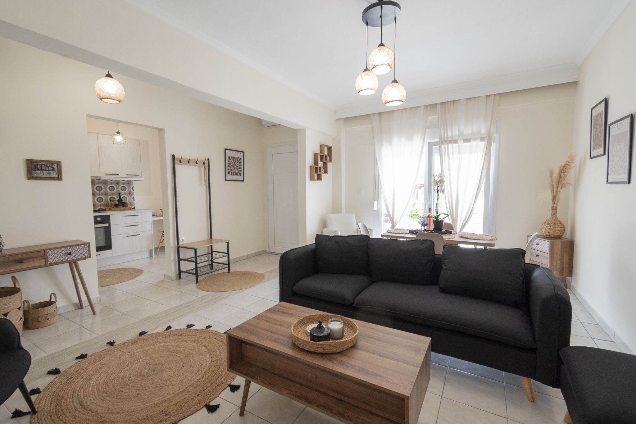 Una sala de estar moderna con un sofá negro, una mesa de centro de madera y un comedor con cocina al fondo.