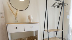 Een kamer met een witte console tafel, een ronde spiegel, een zwart metalen droogrek en een geweven vloerkleed.