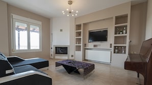 Een woonkamer met een open haard, een aan de muur bevestigde televisie, een piano en een salontafel.