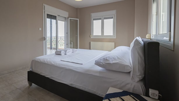 Een slaapkamer met een bed, een raam en een deur naar een balkon.