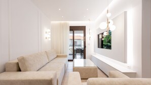 A modern living room with a sofa set, a glass coffee table, and a large TV mounted on the wall.