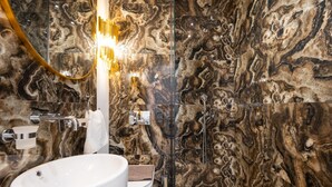 A bathroom with a marble wall, a white sink, and a modern light fixture.