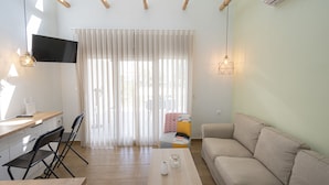 Un salon moderne avec un canapé, une table basse, un téléviseur fixé au mur et une fenêtre avec des rideaux.