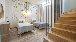 Une chambre avec deux lits, un plancher en bois, un escalier et un mur orné de motifs de feuilles.