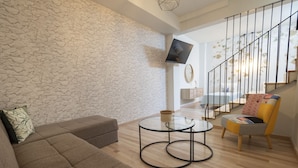 Un salon moderne avec un mur en pierre, un canapé, une table basse en verre, un fauteuil et un escalier.