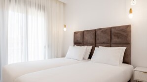 A hotel room with a large bed, white bedding, a brown headboard, and two bedside lamps. - Les Maisons Deluxe Superior by Rentalspro (Kassandra)