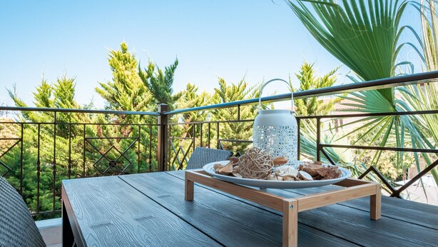 A wooden table with a tray of food and a white lantern on a balcony with metal railings, surrounded by greenery. - Les Maisons Deluxe Superior by Rentalspro (Kassandra)