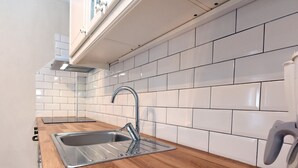 A kitchen with white tiled backsplash, stainless steel sink, wooden countertop, and a kettle. - Fotinia Beach House Ground Floor by Rentalspro (Nea Propontida)
