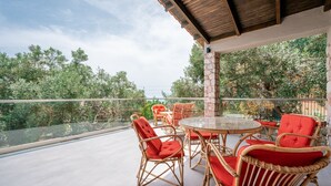 An outdoor patio with wicker furniture and a glass balustrade overlooking a lush garden.
